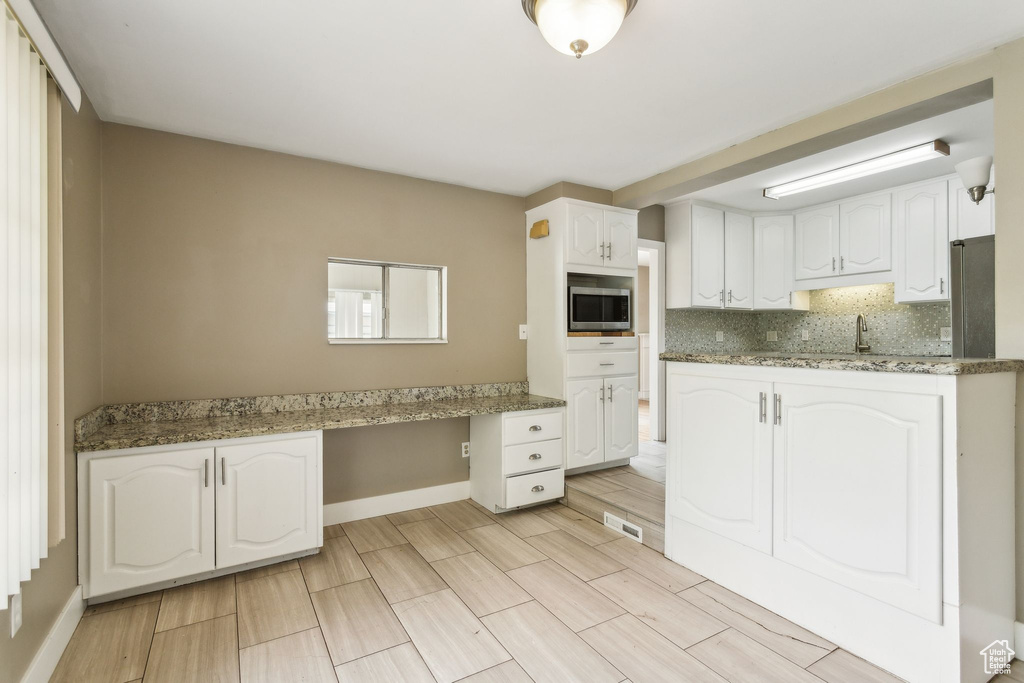 Kitchen featuring white cabinets, stainless steel microwave, baseboards, decorative backsplash, and a sink
