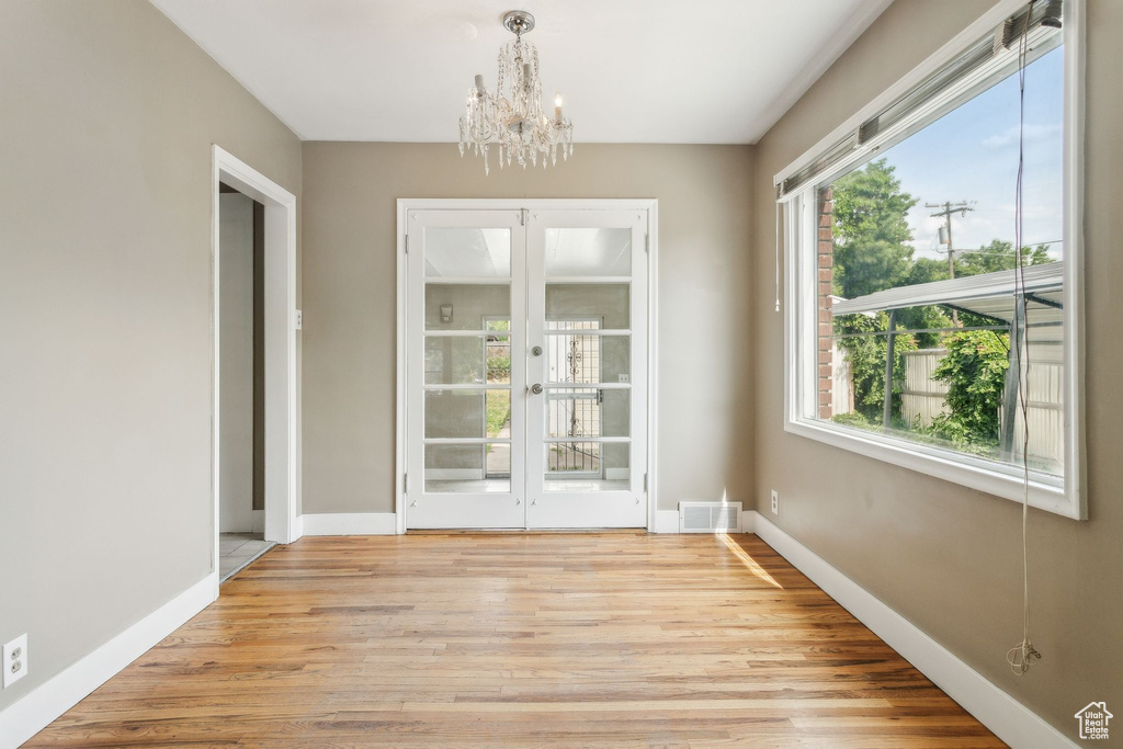 Unfurnished dining area featuring french doors, a chandelier, light wood finished floors, and baseboards
