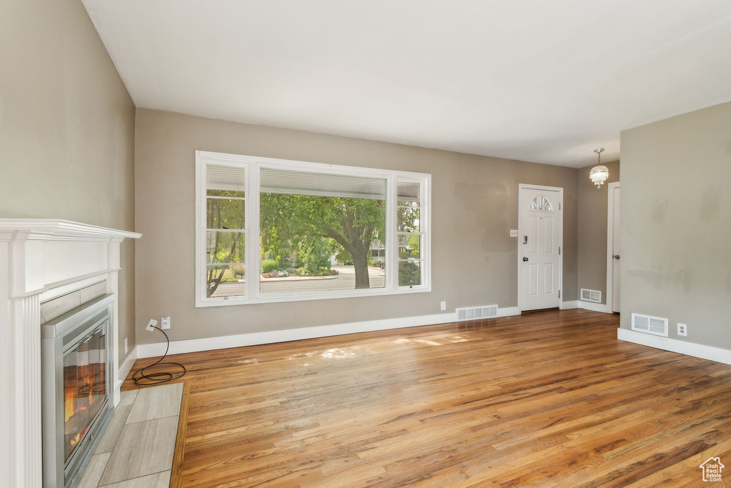 Unfurnished living room featuring baseboards, wood finished floors, a tile fireplace, and a chandelier