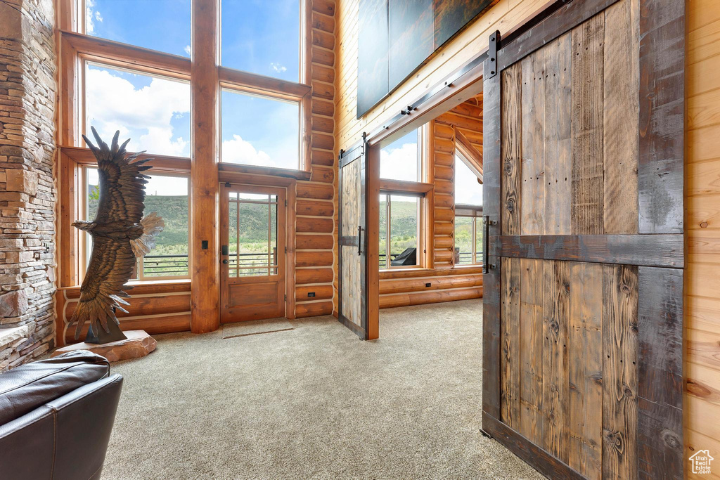 Carpeted foyer entrance with log walls, a towering ceiling, and a barn door
