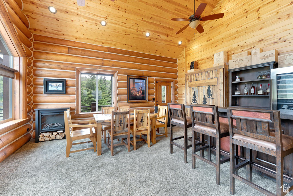 Dining space featuring carpet, ceiling fan, wooden ceiling, high vaulted ceiling, and rustic walls