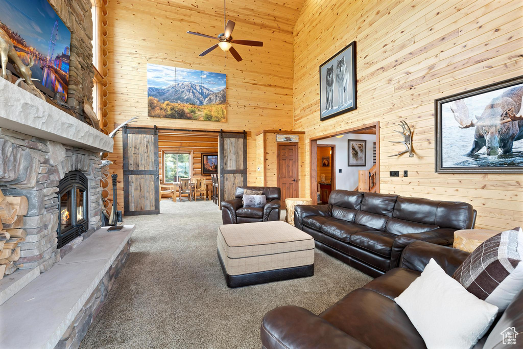 Living room with a high ceiling, wooden walls, carpet, a stone fireplace, and ceiling fan