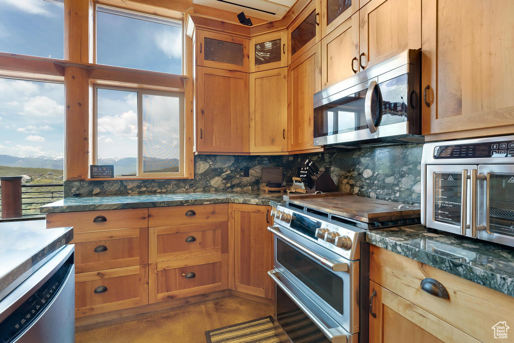 Kitchen with appliances with stainless steel finishes, tasteful backsplash, glass insert cabinets, and dark countertops