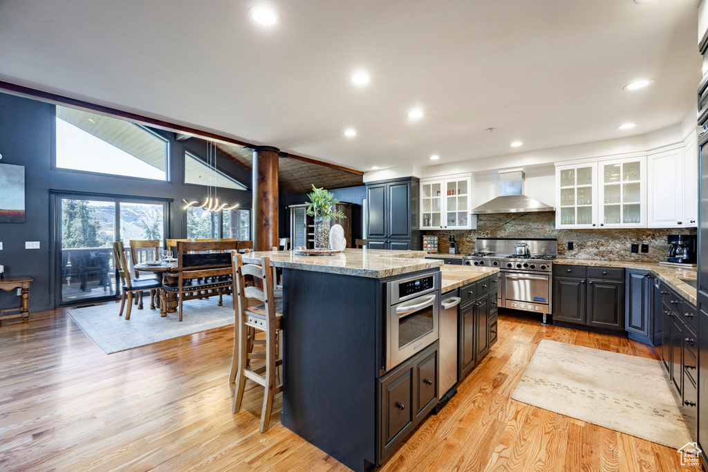 Kitchen featuring wall chimney range hood, appliances with stainless steel finishes, a kitchen island, white cabinetry, and backsplash
