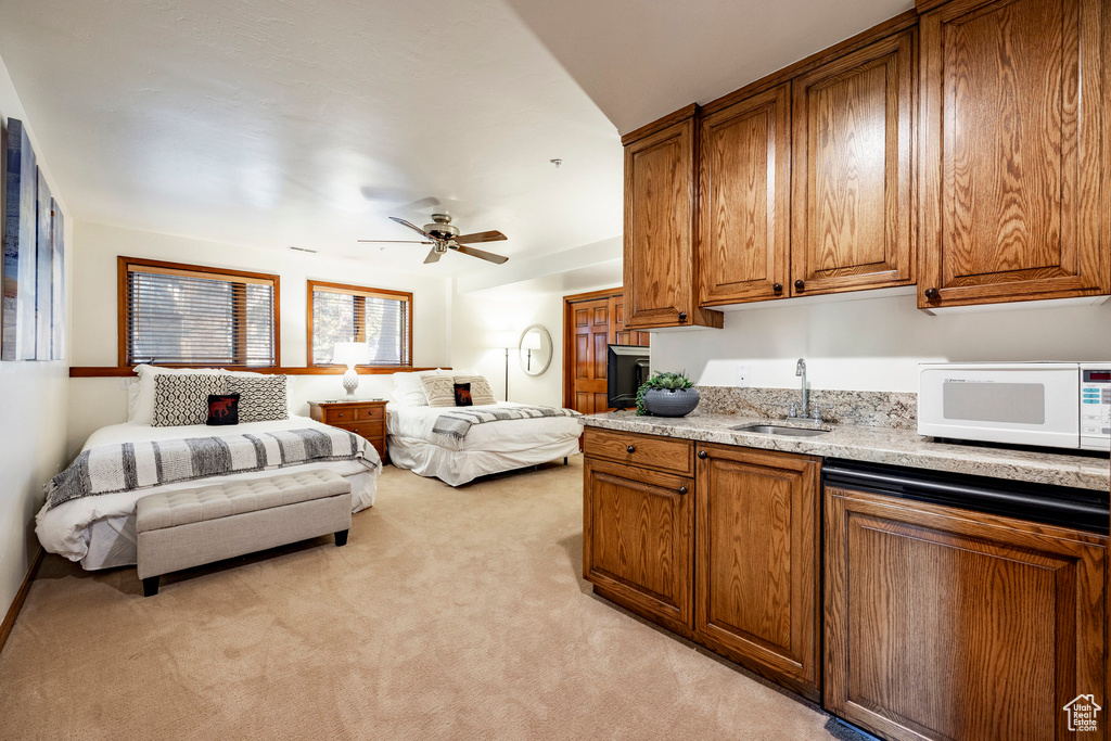 Kitchen with white microwave, a sink, light carpet, brown cabinetry, and ceiling fan
