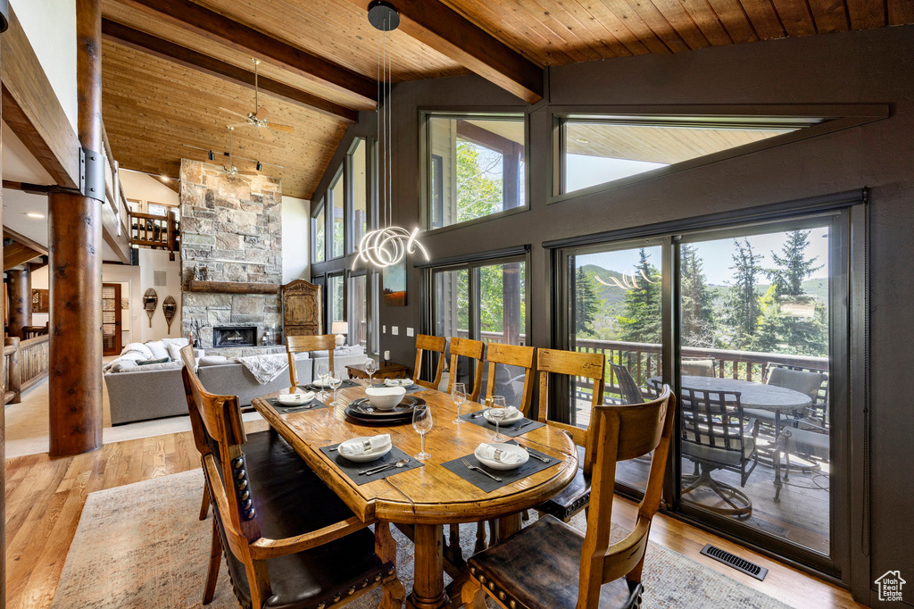 Dining area with a stone fireplace, light wood-type flooring, wooden ceiling with exposed beams, and high vaulted ceiling