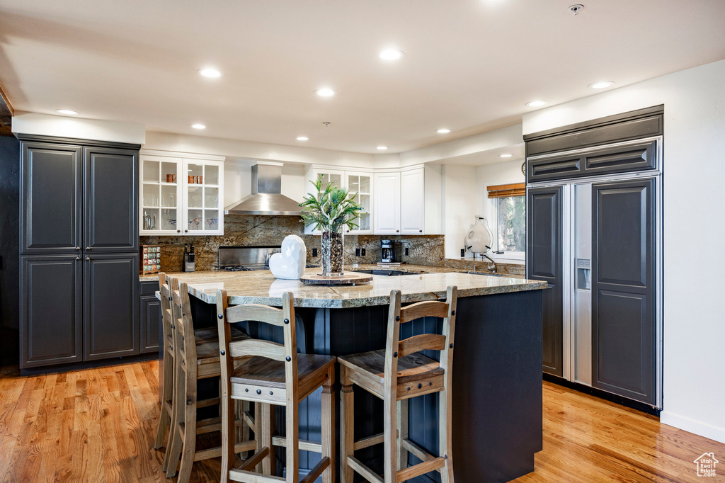 Kitchen with paneled built in refrigerator, wall chimney exhaust hood, a kitchen island, a kitchen breakfast bar, and white cabinets