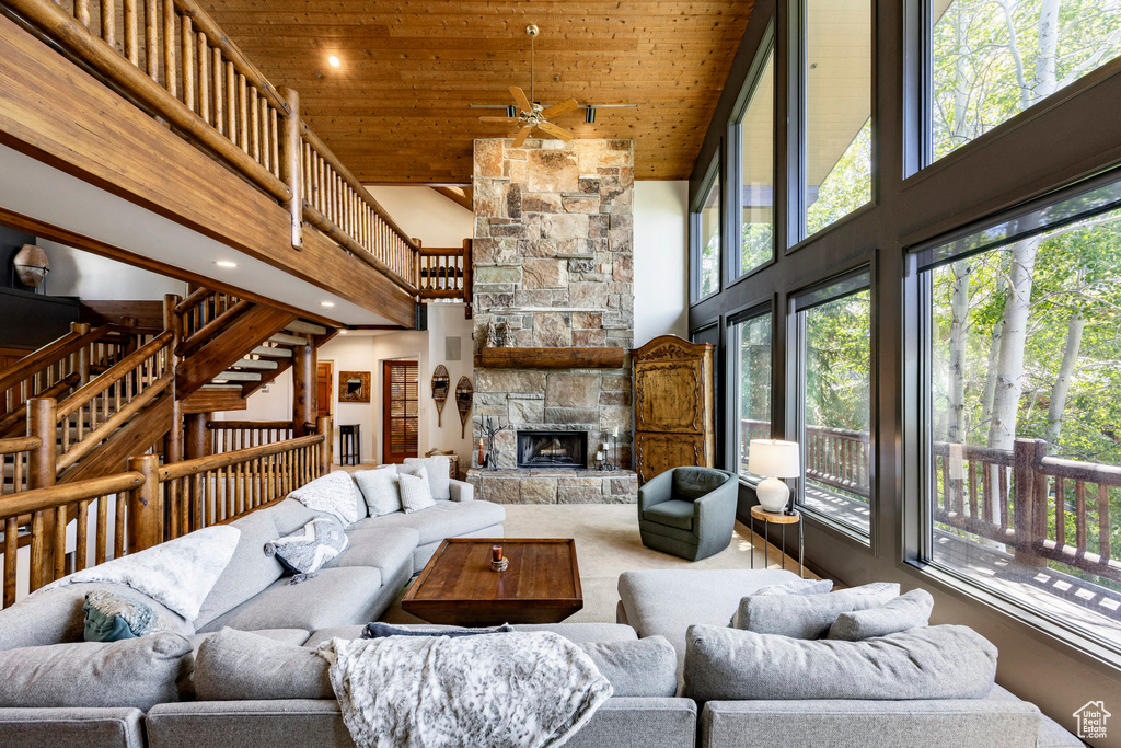 Living room with high vaulted ceiling, wood ceiling, a ceiling fan, a stone fireplace, and stairway