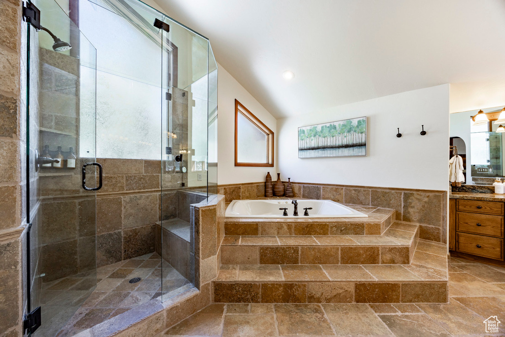 Bathroom featuring vanity, a garden tub, stone tile flooring, a stall shower, and vaulted ceiling