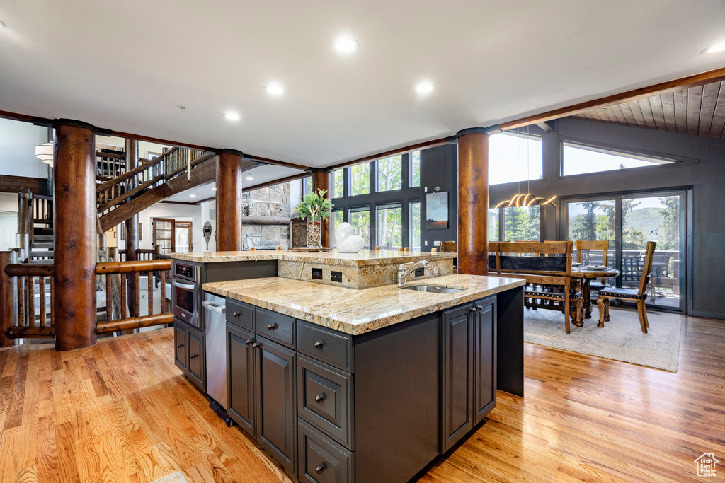Kitchen featuring a sink, light wood-style flooring, light stone countertops, an island with sink, and recessed lighting