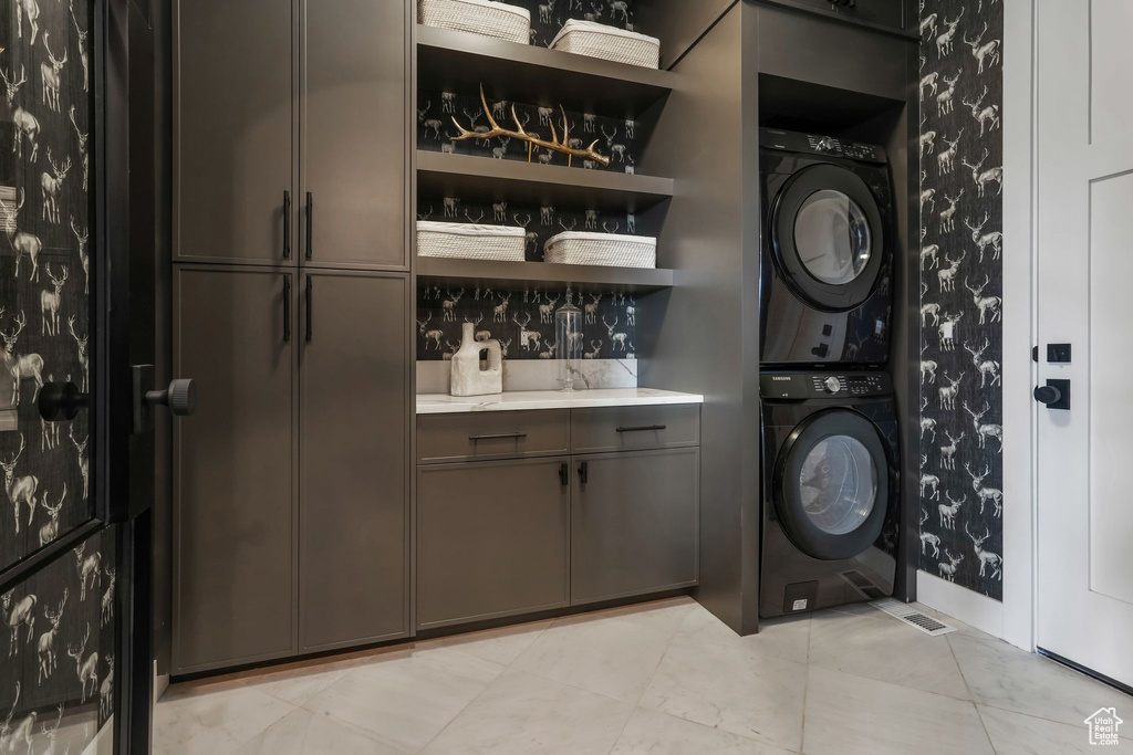 Laundry area with stacked washer / dryer, wallpapered walls, and cabinet space