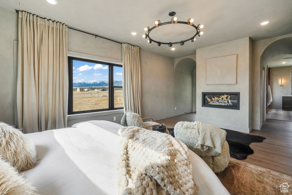 Bedroom featuring arched walkways, wood finished floors, recessed lighting, and a glass covered fireplace
