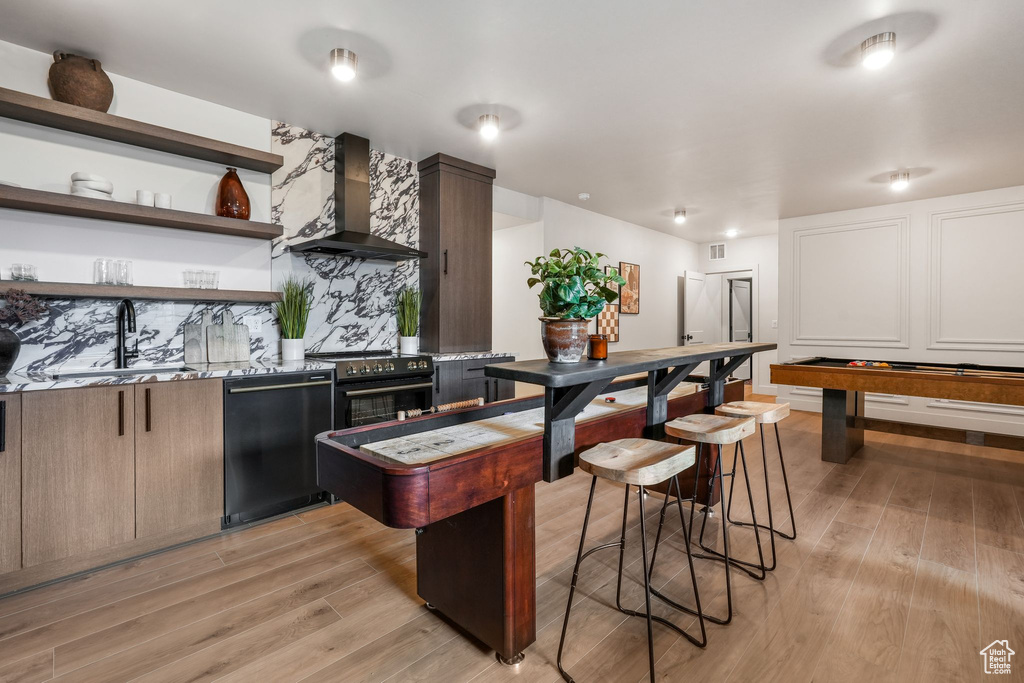 Kitchen with wall chimney range hood, dishwasher, a sink, high end range, and light wood-type flooring
