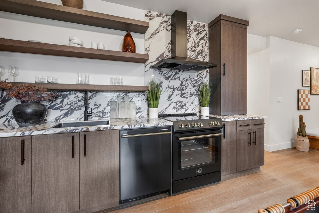 Kitchen featuring range with electric stovetop, wall chimney exhaust hood, dishwashing machine, open shelves, and light wood-style floors