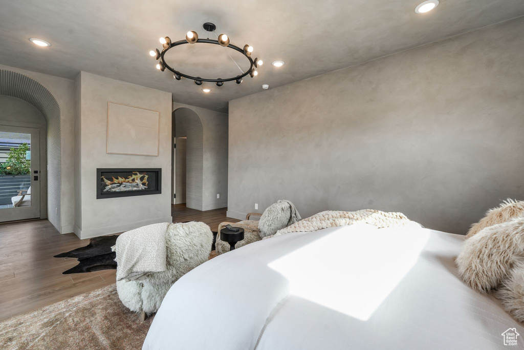 Bedroom with arched walkways, wood finished floors, access to exterior, a glass covered fireplace, and recessed lighting