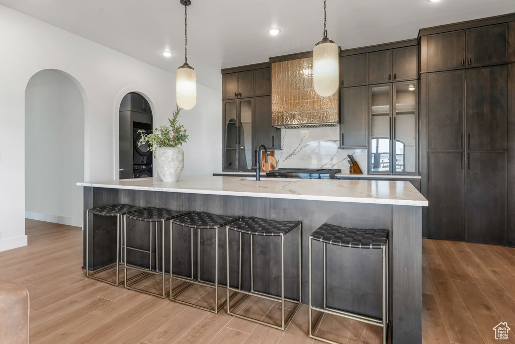 Kitchen with light wood finished floors, a breakfast bar area, backsplash, dark brown cabinets, and a large island