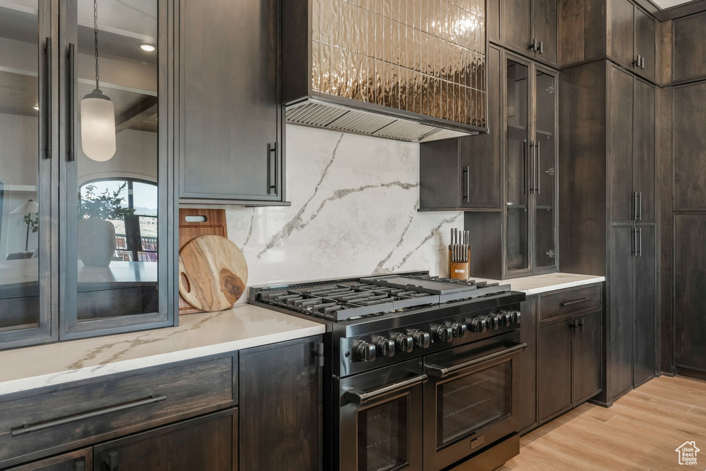 Kitchen with range with two ovens, dark brown cabinets, backsplash, glass insert cabinets, and light wood-style flooring