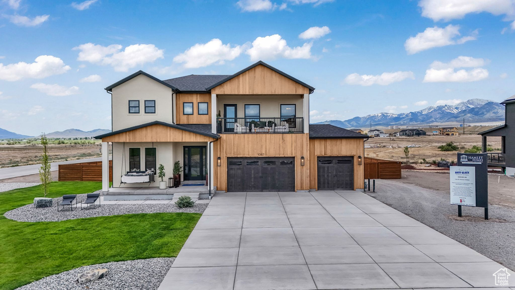 Contemporary house featuring a mountain view, a balcony, driveway, an attached garage, and roof with shingles