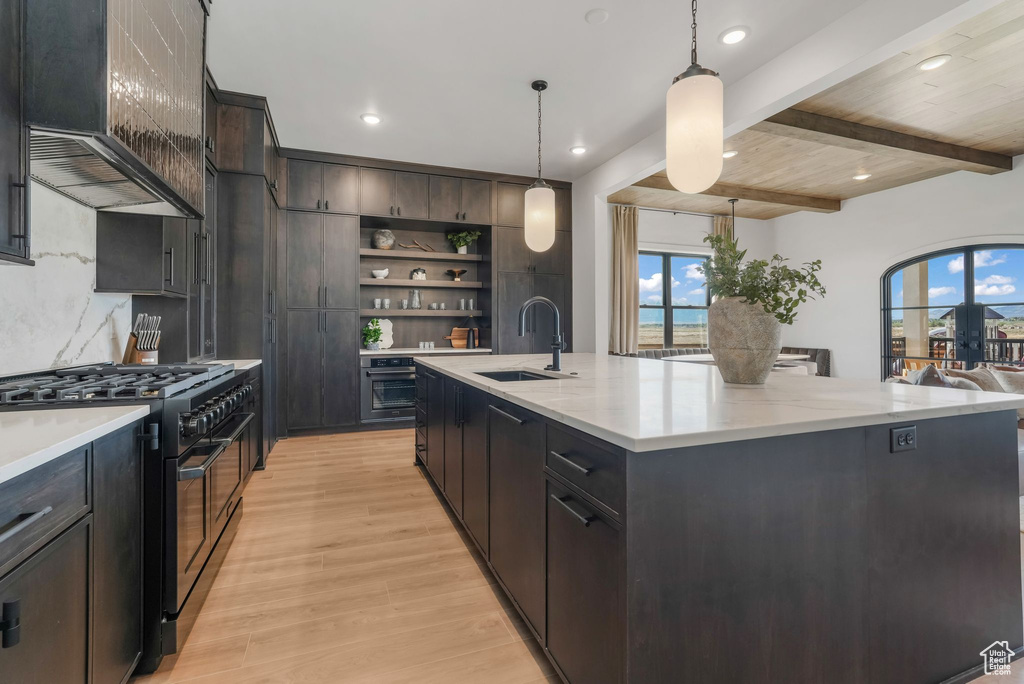 Kitchen featuring a sink, double oven range, custom range hood, open shelves, and light wood-type flooring