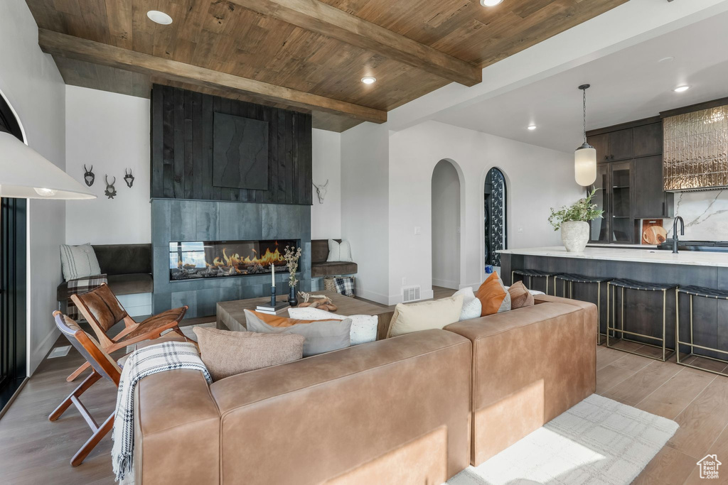 Living area featuring arched walkways, wooden ceiling with exposed beams, light wood-style floors, recessed lighting, and a multi sided fireplace