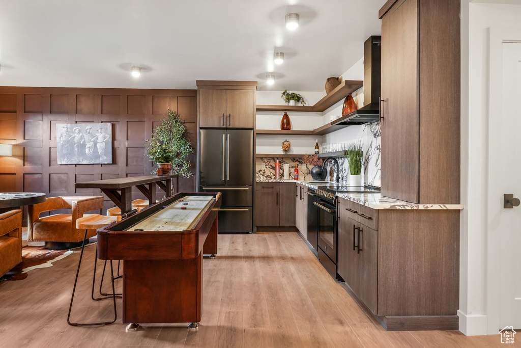 Kitchen featuring high quality fridge, black range with electric stovetop, wall chimney exhaust hood, open shelves, and light wood-style flooring
