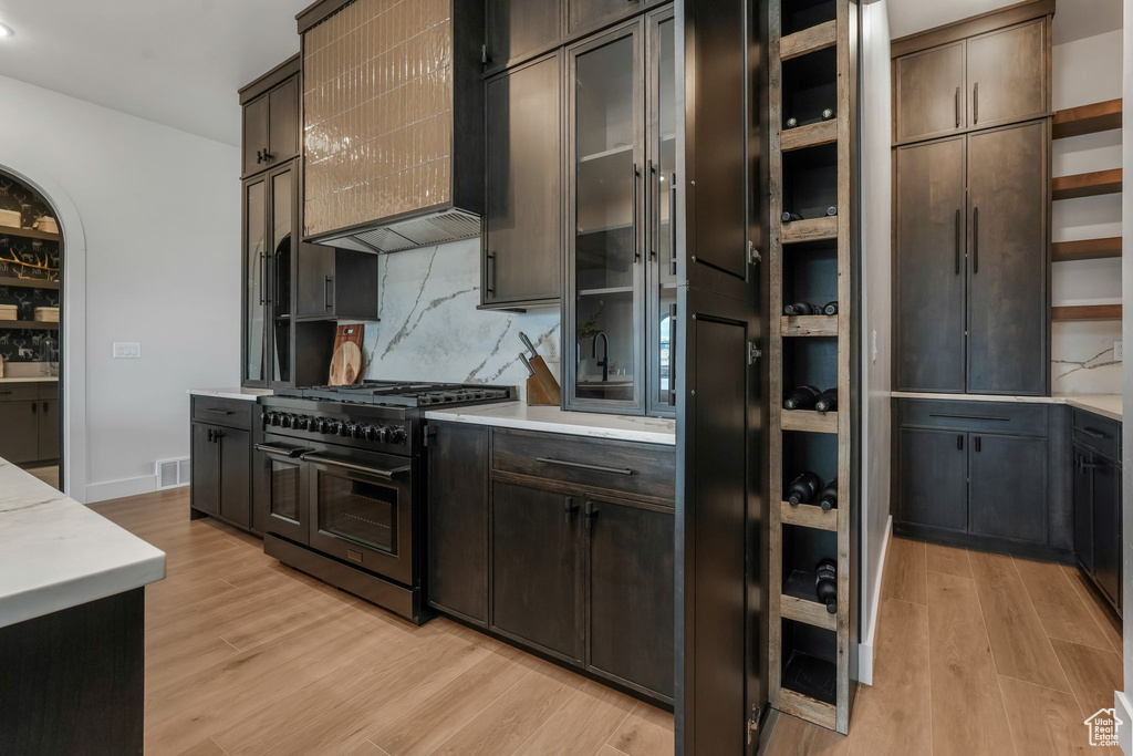 Kitchen featuring high end black range, open shelves, light countertops, tasteful backsplash, and light wood finished floors