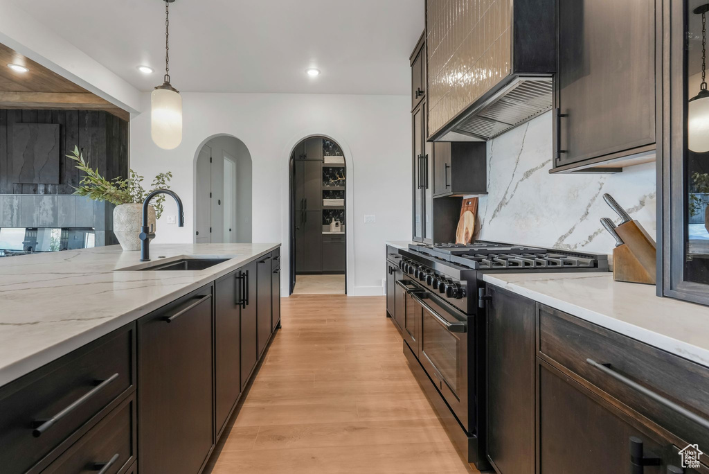 Kitchen with range with two ovens, a sink, wall chimney range hood, arched walkways, and tasteful backsplash