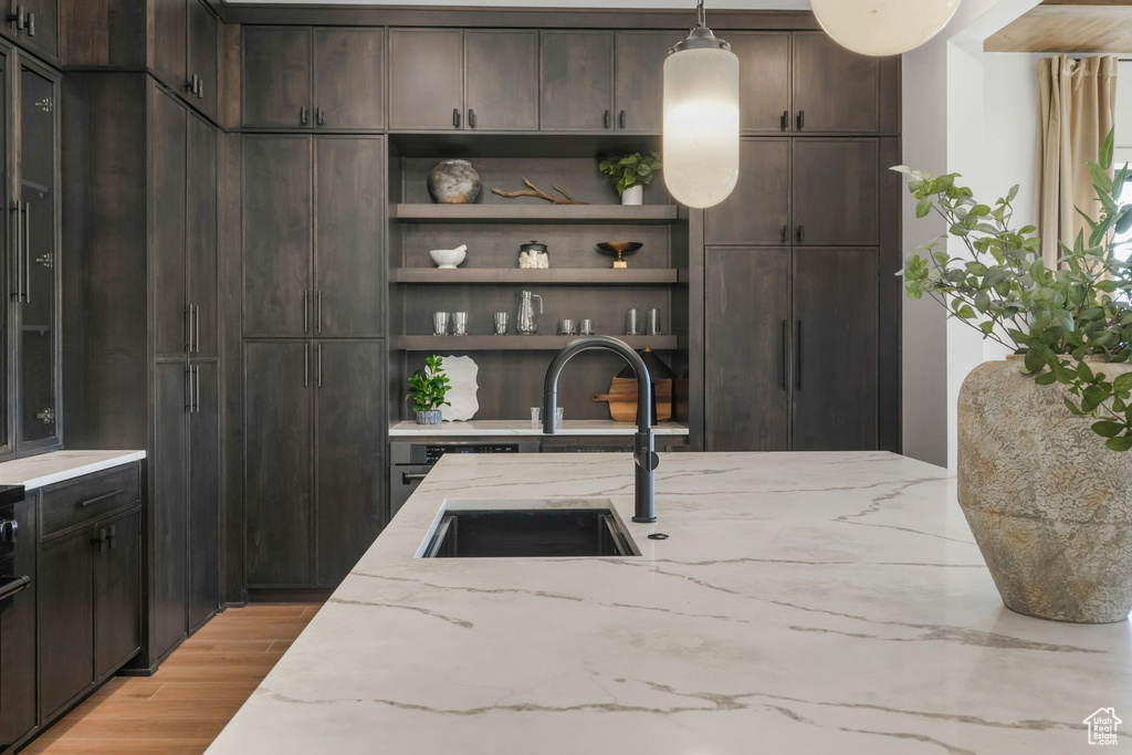 Kitchen with a sink, dark brown cabinets, light wood-type flooring, and light stone counters