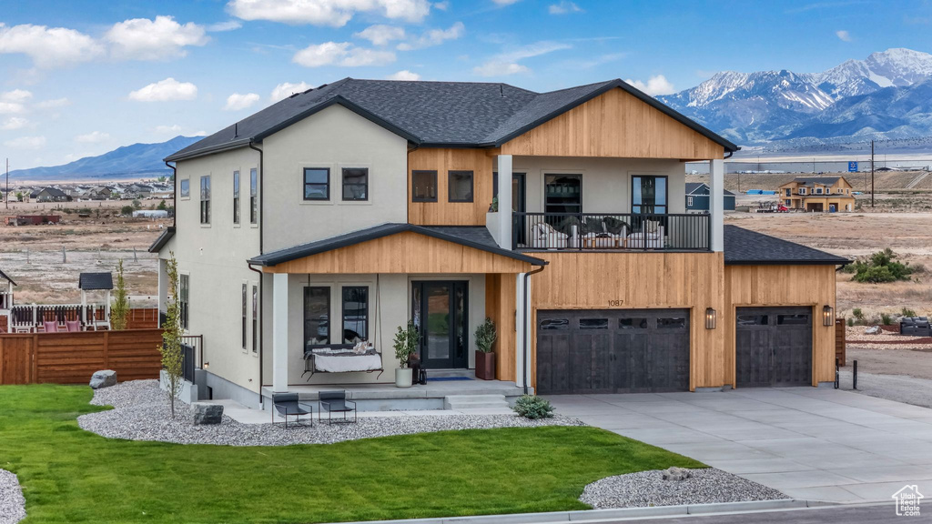 Modern home featuring a mountain view, a balcony, driveway, a garage, and a front yard