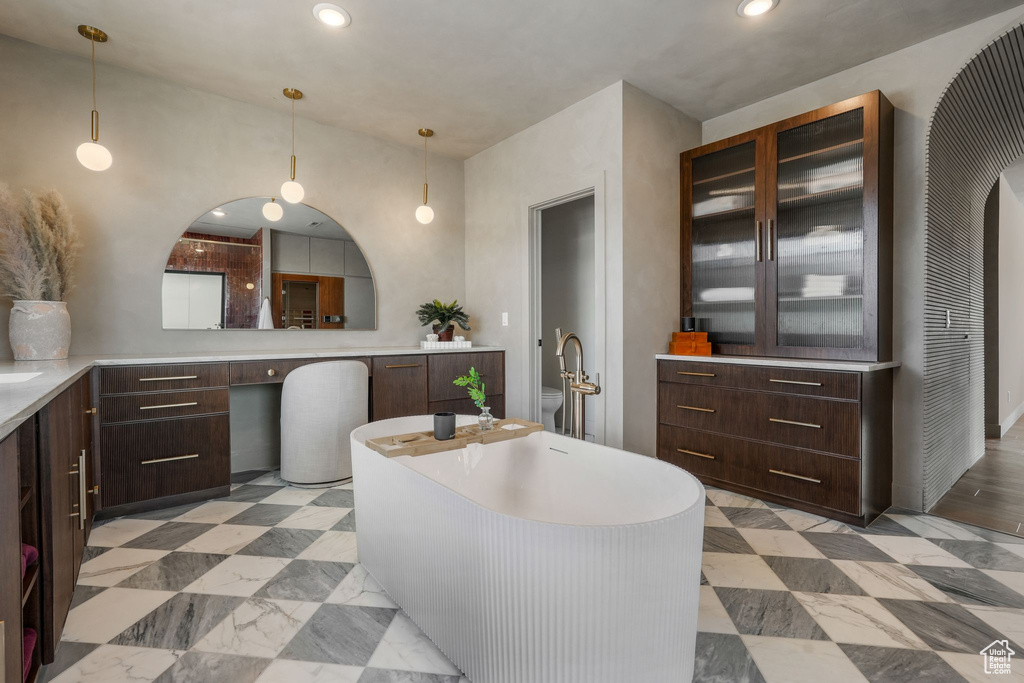 Kitchen with dark brown cabinets, glass insert cabinets, recessed lighting, light countertops, and pendant lighting