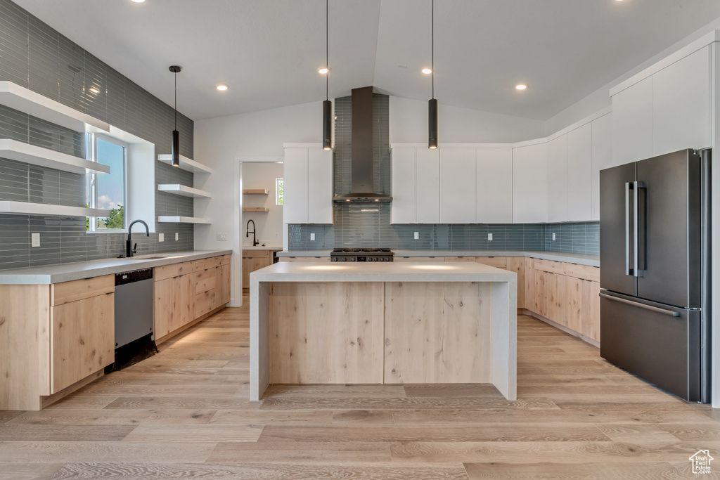 Kitchen with high quality fridge, light brown cabinets, stainless steel dishwasher, wall chimney exhaust hood, and vaulted ceiling