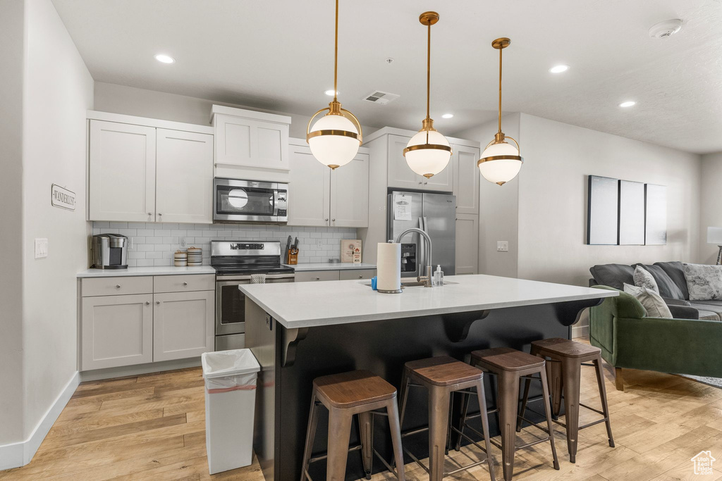Kitchen featuring appliances with stainless steel finishes, a sink, backsplash, light countertops, and open floor plan