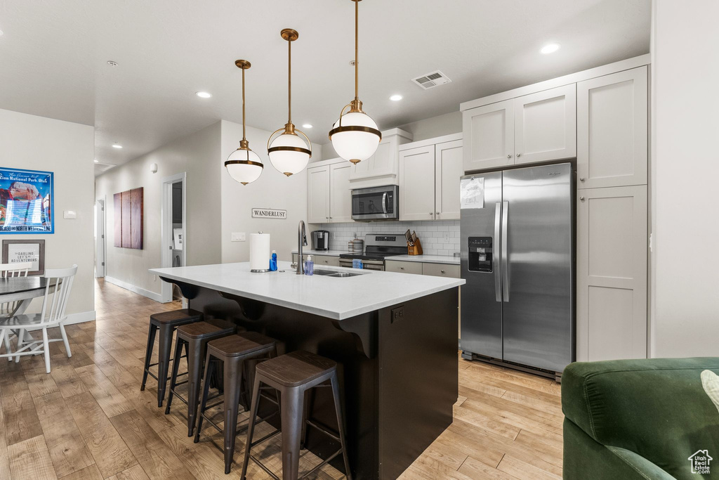 Kitchen with appliances with stainless steel finishes, a sink, a breakfast bar area, tasteful backsplash, and light wood-type flooring