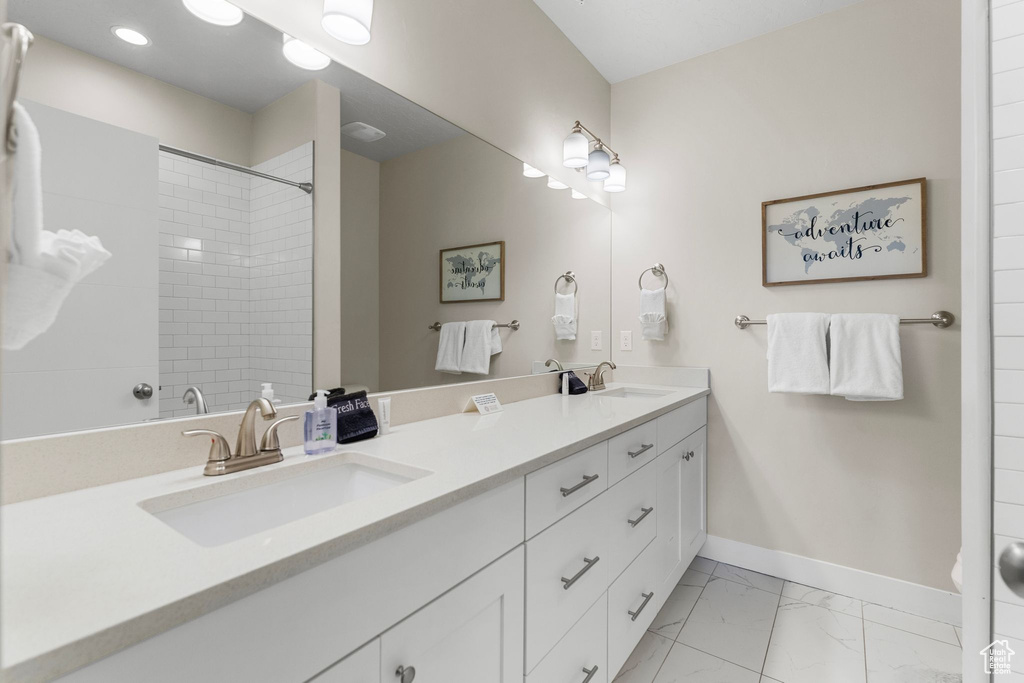 Bathroom featuring marble look tile flooring, double vanity, baseboards, a tile shower, and recessed lighting