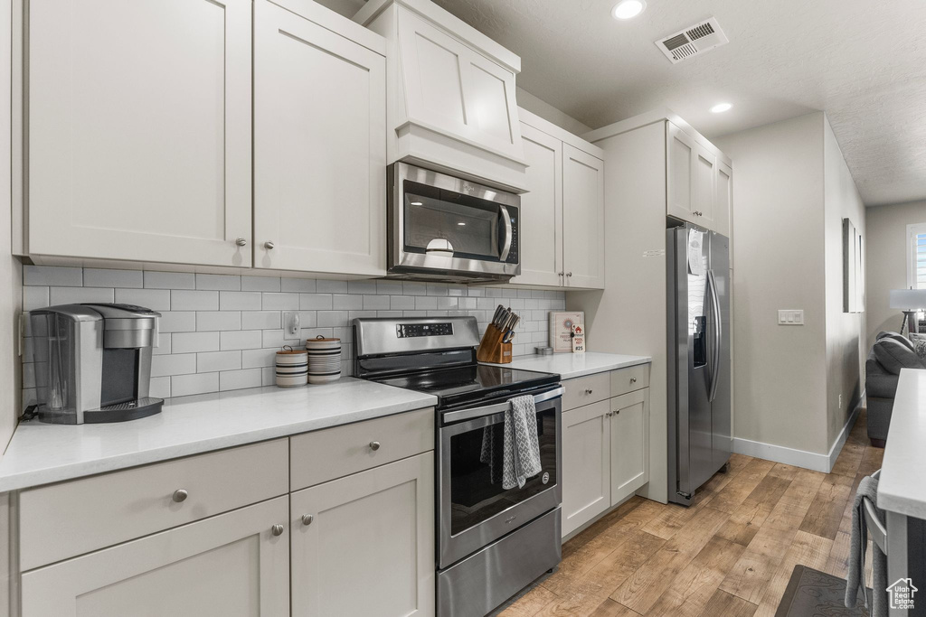 Kitchen with appliances with stainless steel finishes, light wood-style floors, tasteful backsplash, recessed lighting, and baseboards