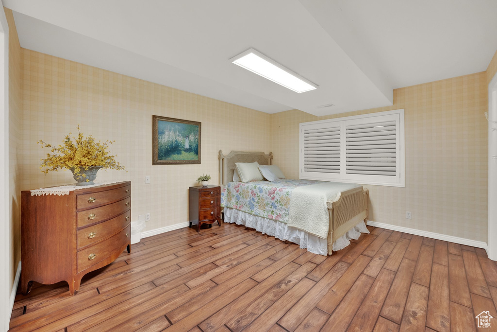 Bedroom with wallpapered walls, light wood-type flooring, and baseboards