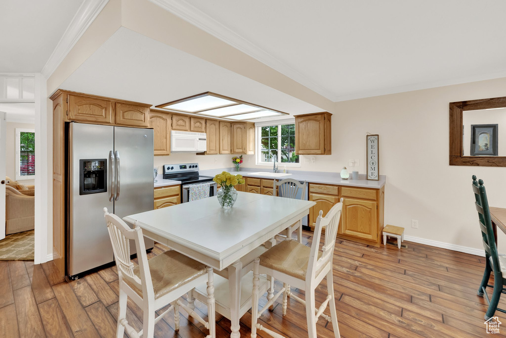 Kitchen with stainless steel appliances, a sink, light wood-style floors, crown molding, and light countertops