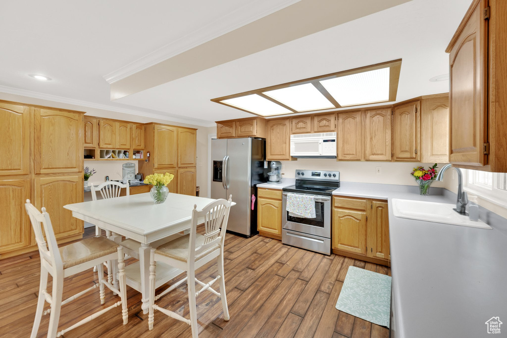 Kitchen featuring appliances with stainless steel finishes, light wood finished floors, a sink, light countertops, and ornamental molding