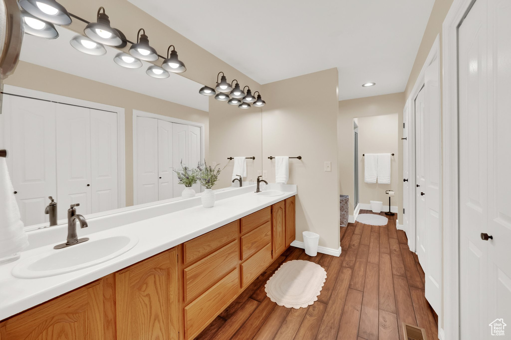 Bathroom featuring a closet, double vanity, hardwood / wood-style floors, baseboards, and recessed lighting