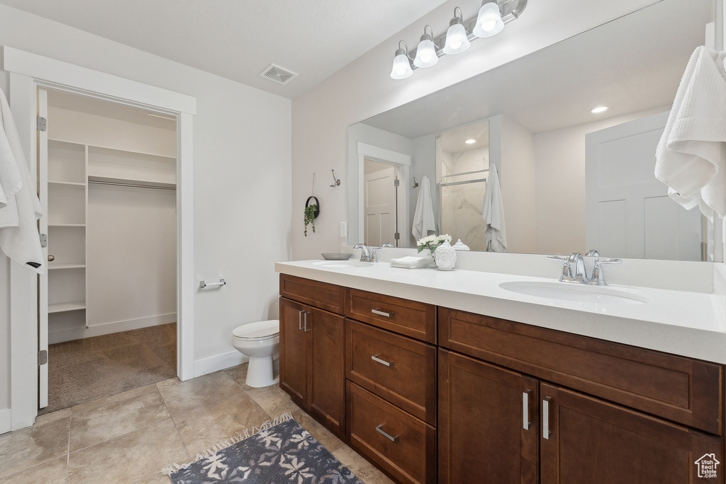 Full bath with double vanity, a shower with door, toilet, a walk in closet, and baseboards