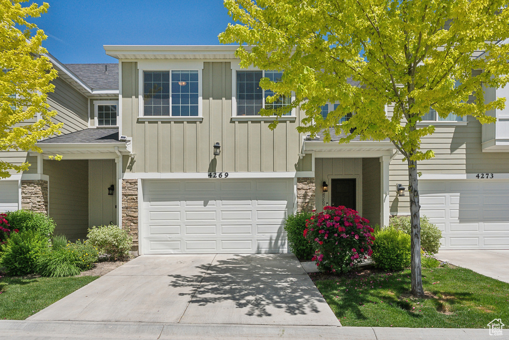 View of front of home featuring stone siding, board and batten siding, a garage, driveway, and roof with shingles