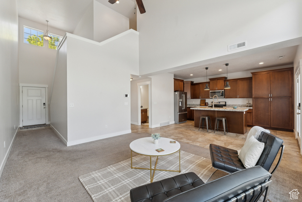 Living area with a towering ceiling, baseboards, recessed lighting, a ceiling fan, and light carpet