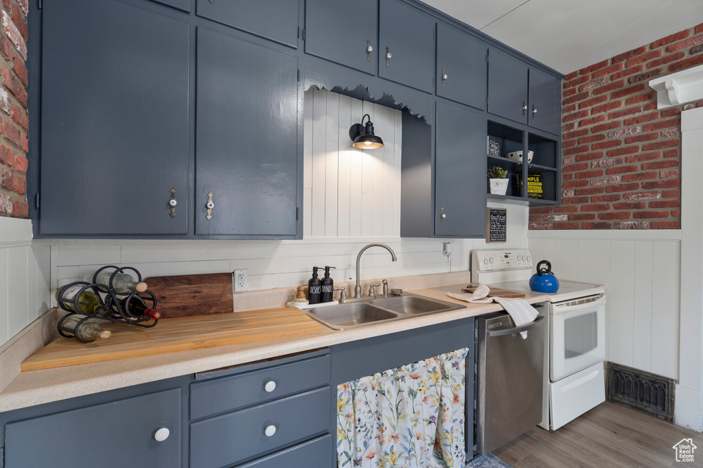 Kitchen featuring a sink, electric range, blue cabinetry, brick wall, and light countertops