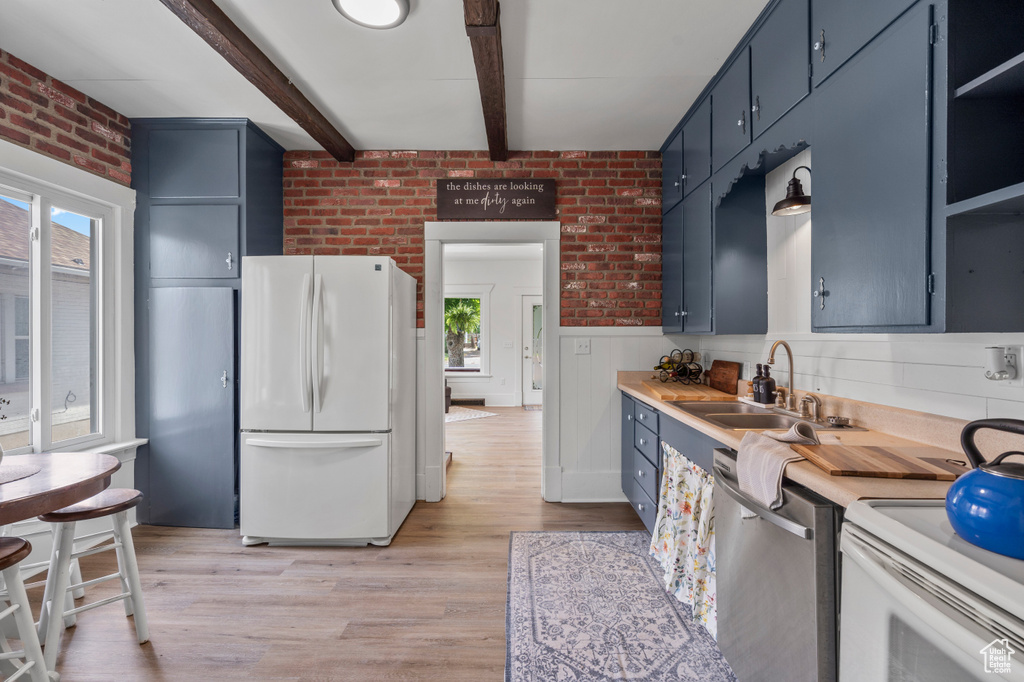 Kitchen with freestanding refrigerator, dishwasher, a sink, blue cabinets, and brick wall