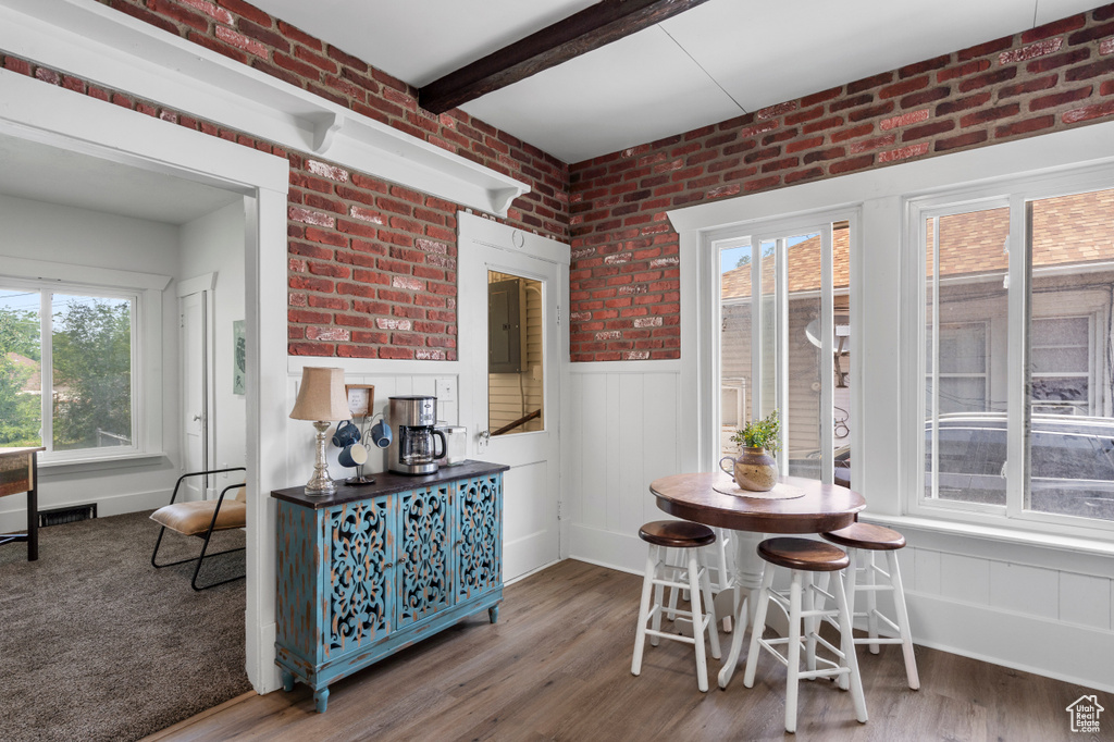 Dining space with wood finished floors, a wainscoted wall, brick wall, and beam ceiling