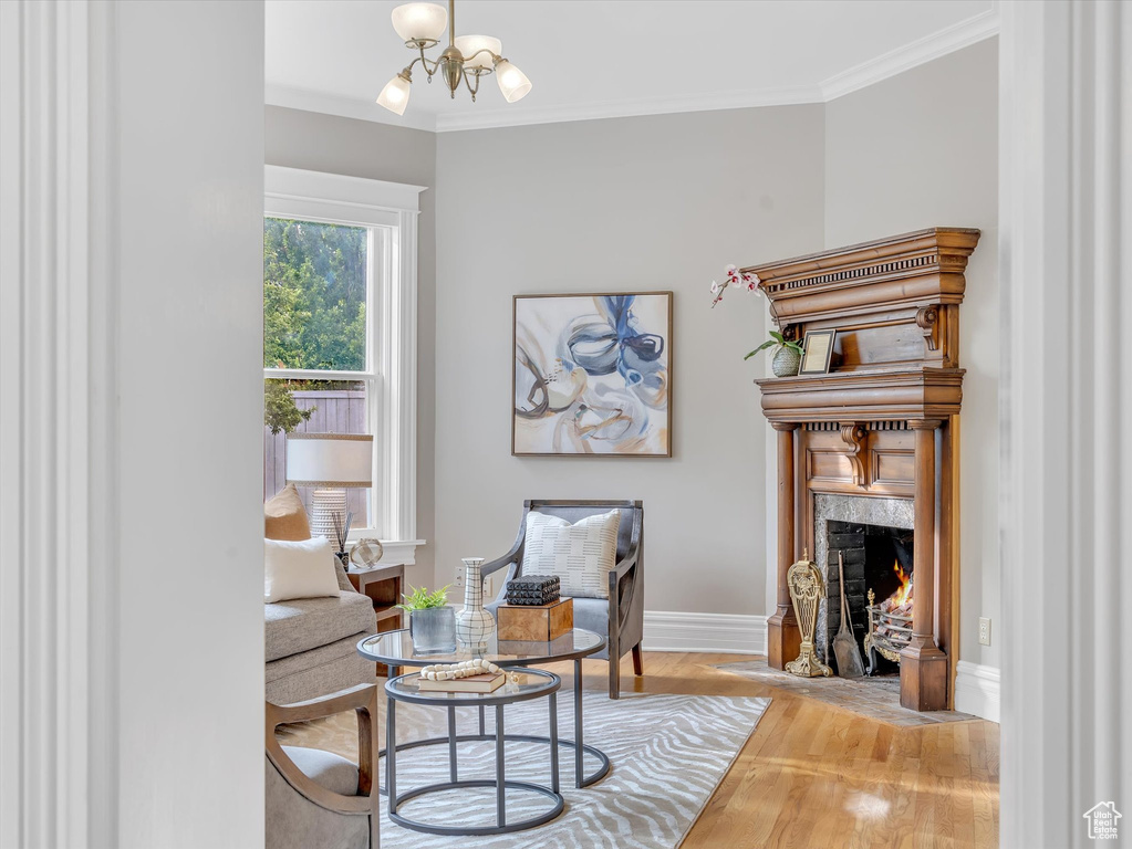 Sitting room with a premium fireplace, wood finished floors, a chandelier, baseboards, and ornamental molding