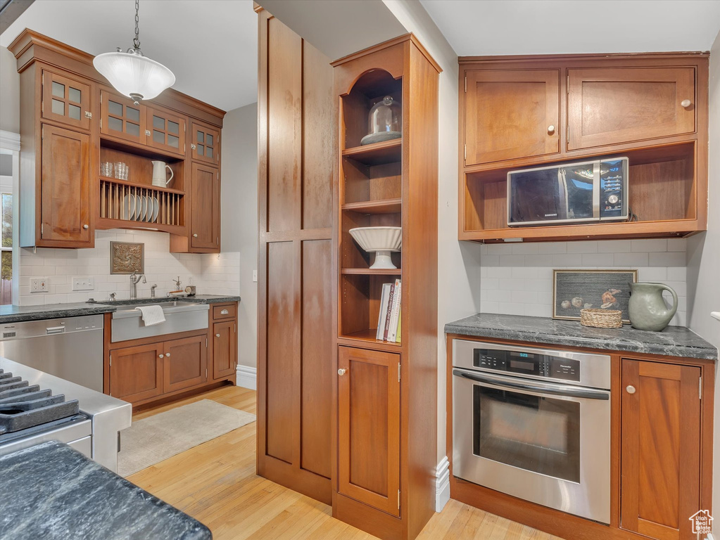 Kitchen featuring stainless steel appliances, open shelves, light wood-type flooring, brown cabinetry, and a sink