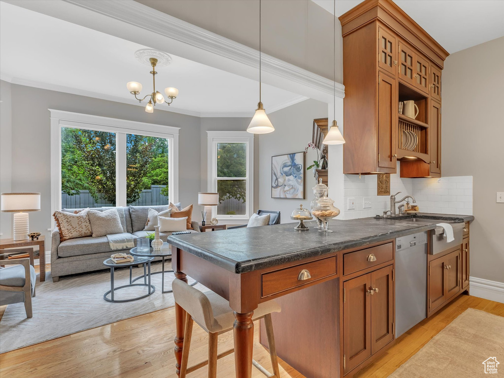 Kitchen featuring stainless steel dishwasher, brown cabinets, pendant lighting, light wood-style floors, and crown molding