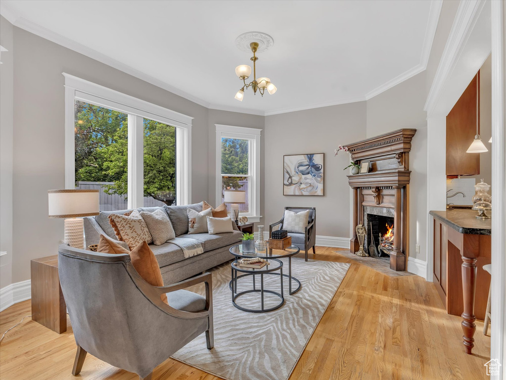 Living area featuring a fireplace, crown molding, a chandelier, light wood-style flooring, and baseboards