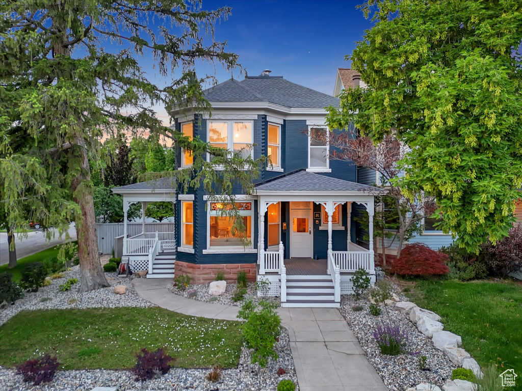 View of front of home with a porch, roof with shingles, a front lawn, and stairs